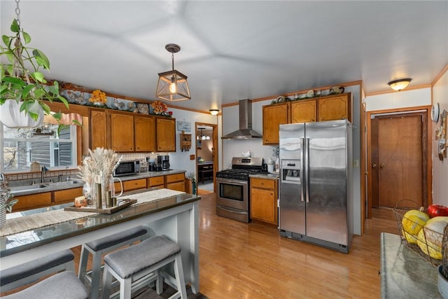 kitchen featuring appliances with stainless steel finishes, decorative light fixtures, crown molding, wall chimney range hood, and light hardwood / wood-style flooring