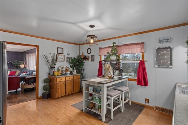 dining room featuring ornamental molding, lofted ceiling, and light hardwood / wood-style flooring