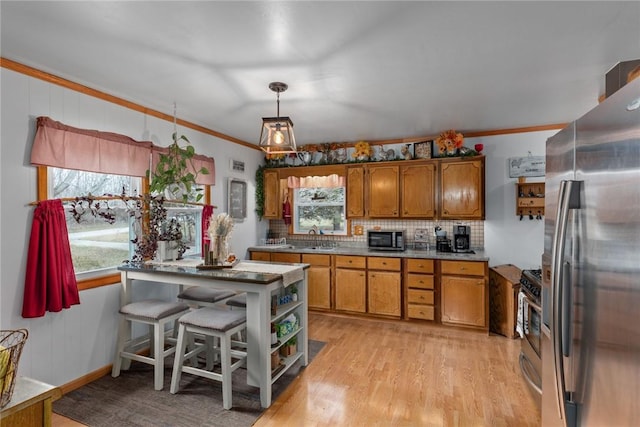 kitchen with sink, stainless steel appliances, ornamental molding, light hardwood / wood-style floors, and decorative light fixtures