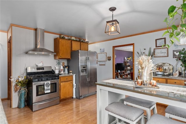 kitchen featuring pendant lighting, wall chimney range hood, crown molding, appliances with stainless steel finishes, and light wood-type flooring