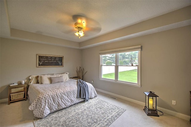 carpeted bedroom with visible vents, a ceiling fan, baseboards, and a tray ceiling