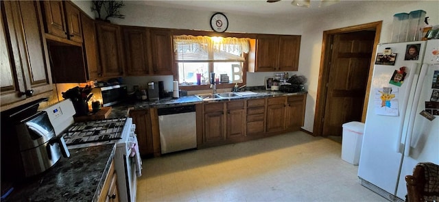 kitchen featuring brown cabinets, light floors, stainless steel appliances, dark countertops, and a sink