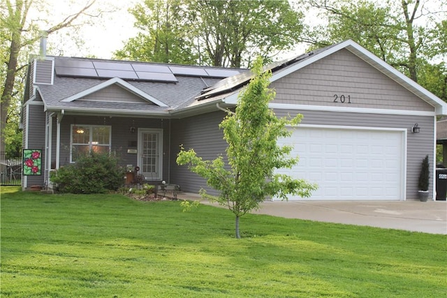 view of front of home featuring a front lawn, an attached garage, roof mounted solar panels, concrete driveway, and a shingled roof