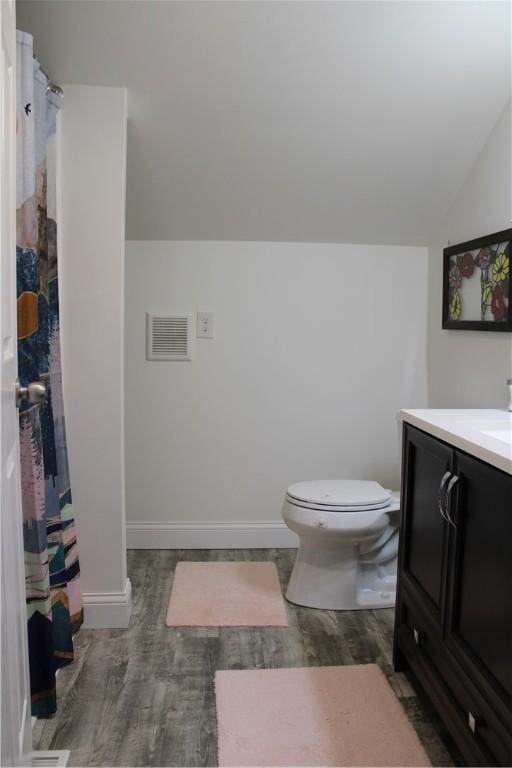 bathroom featuring toilet, lofted ceiling, wood finished floors, vanity, and baseboards