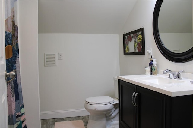 bathroom with lofted ceiling, vanity, toilet, wood finished floors, and baseboards