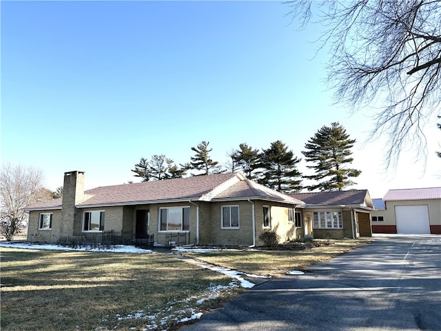 ranch-style home featuring aphalt driveway, a front yard, a chimney, and a garage