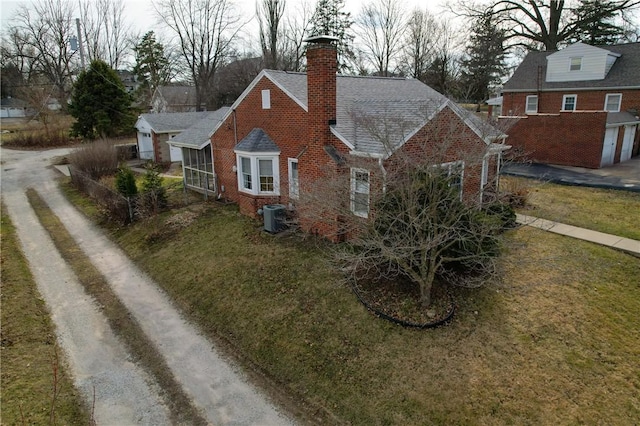 view of front of house with central air condition unit, a front lawn, dirt driveway, brick siding, and a chimney