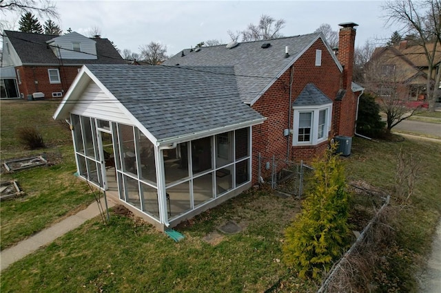 rear view of house with roof with shingles, a yard, a sunroom, a chimney, and brick siding