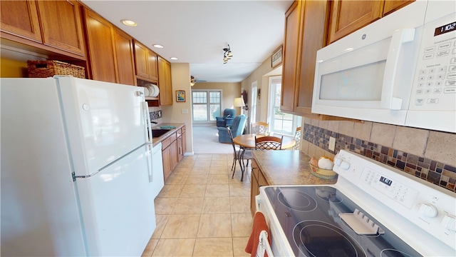 kitchen with backsplash, ceiling fan, light tile patterned floors, brown cabinets, and white appliances