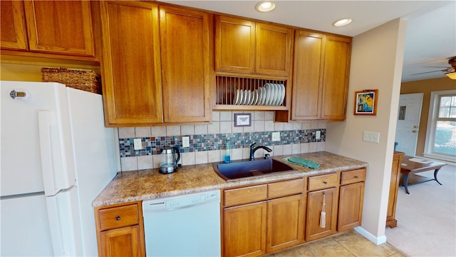 kitchen featuring brown cabinets, a sink, light stone counters, backsplash, and white appliances