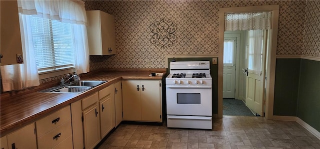 kitchen with cream cabinetry, wood counters, white gas range, and sink