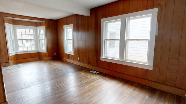 empty room with beam ceiling, wooden walls, and hardwood / wood-style flooring