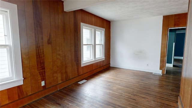 empty room featuring beamed ceiling, hardwood / wood-style flooring, and wood walls