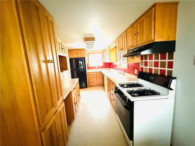 314 W Maple St, Hoopeston, IL 60942 - kitchen with freestanding refrigerator, gas range oven, under cabinet range hood, brown cabinetry, and light countertops