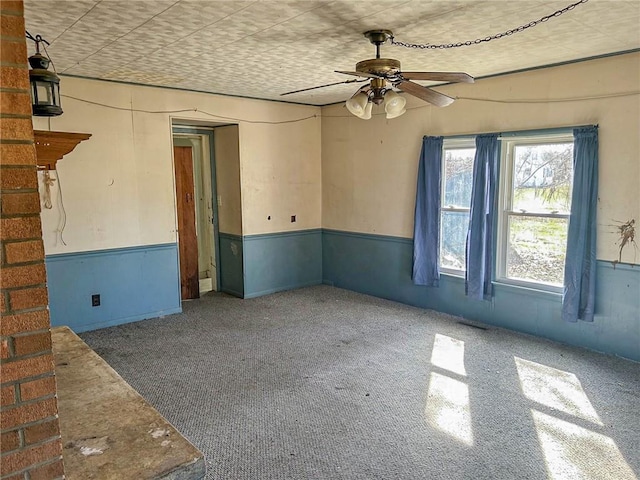 unfurnished room with carpet floors, a ceiling fan, and wainscoting