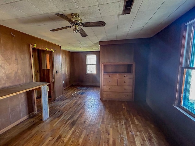interior space featuring wood-type flooring, a ceiling fan, wood walls, and visible vents