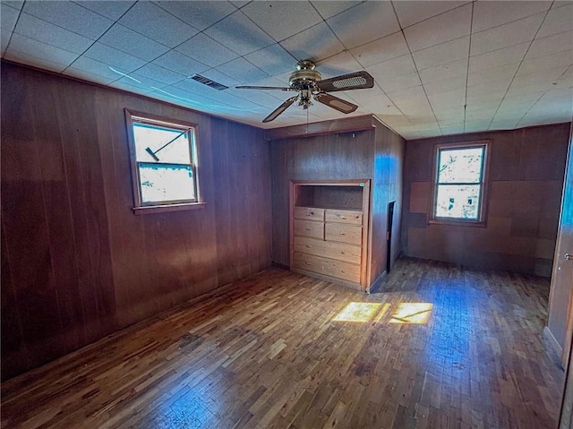 unfurnished bedroom with wood finished floors, wooden walls, multiple windows, and visible vents