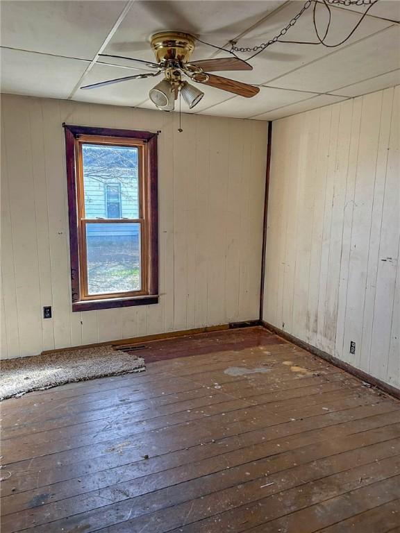 unfurnished room featuring hardwood / wood-style floors, baseboards, wooden walls, and a ceiling fan