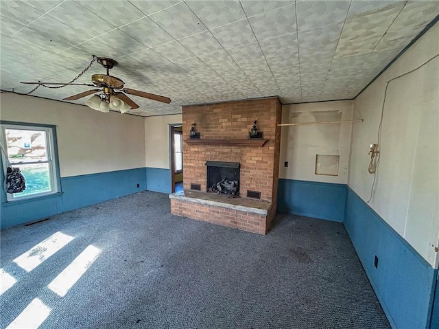 unfurnished living room featuring carpet, a wainscoted wall, ceiling fan, visible vents, and a fireplace