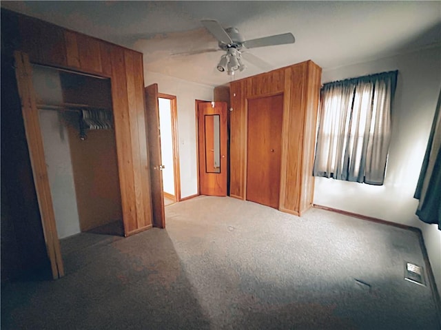 unfurnished bedroom featuring baseboards, carpet floors, two closets, and ceiling fan