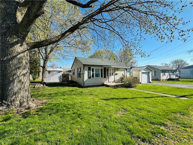 view of front facade featuring aphalt driveway, metal roof, an attached garage, an outdoor structure, and a front yard