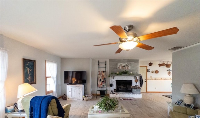 living area featuring light wood-style flooring, a fireplace, visible vents, and baseboards