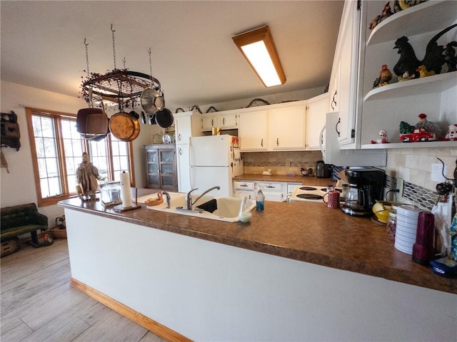 kitchen featuring white appliances, a peninsula, open shelves, a sink, and light wood-style floors