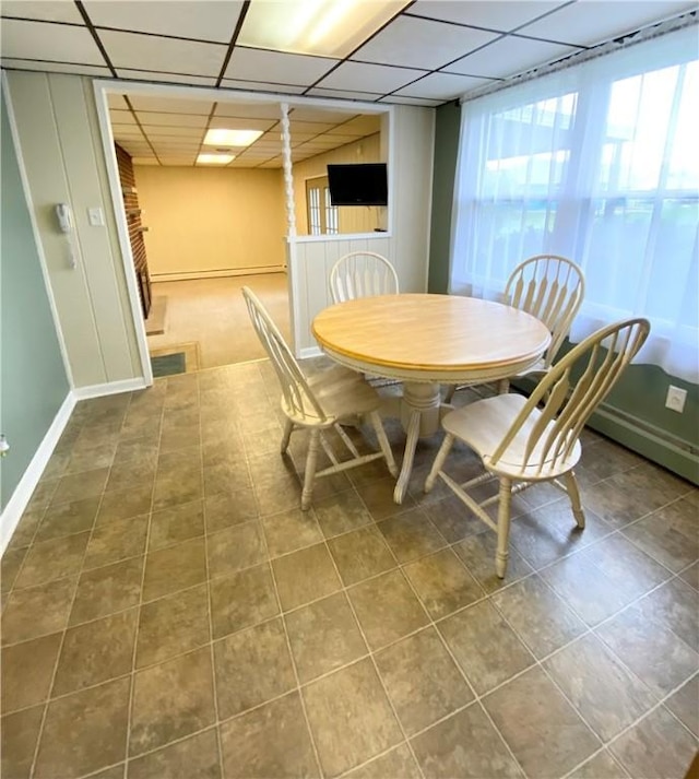 tiled dining area featuring a paneled ceiling and baseboards