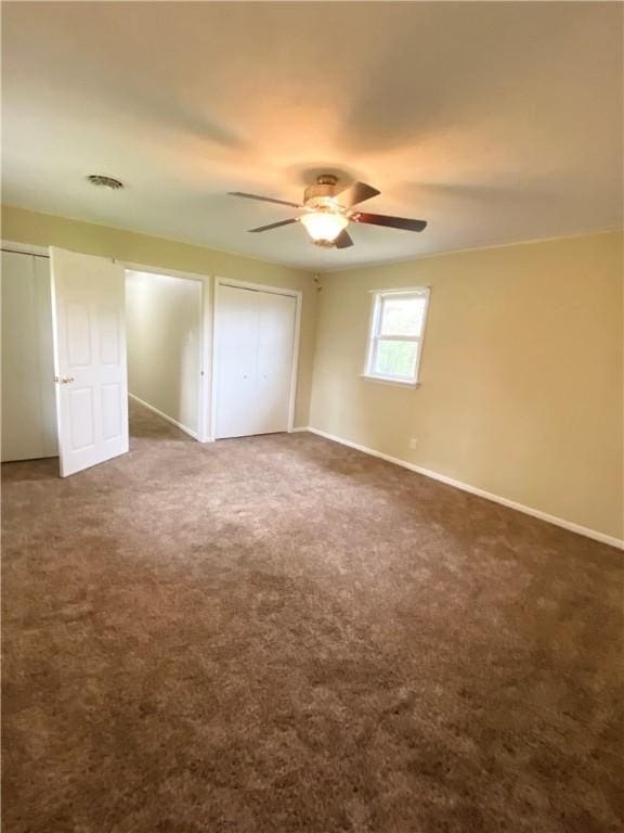 unfurnished bedroom featuring dark colored carpet, visible vents, a ceiling fan, and baseboards