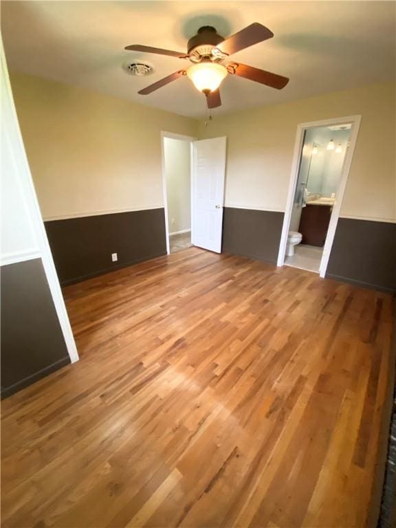 unfurnished bedroom featuring visible vents, ensuite bathroom, wood finished floors, and a ceiling fan
