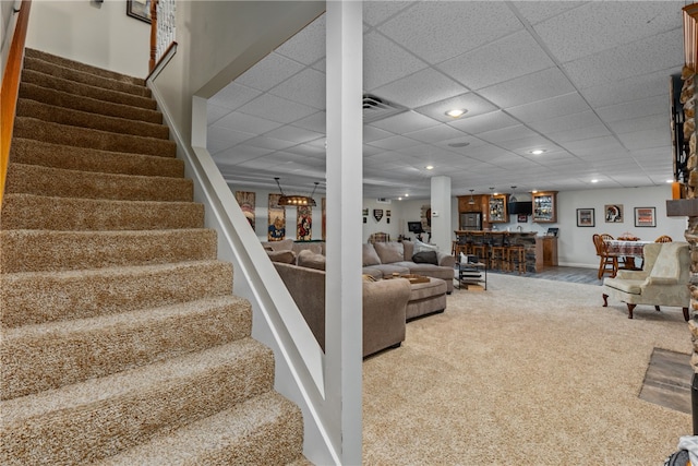 carpeted living room featuring bar and a drop ceiling