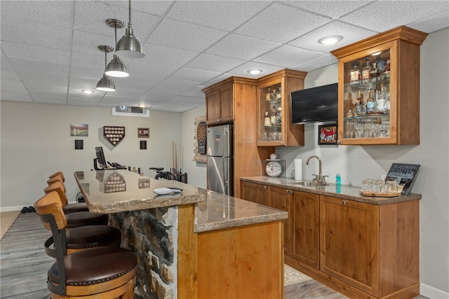 bar featuring pendant lighting, a paneled ceiling, sink, light stone countertops, and stainless steel refrigerator