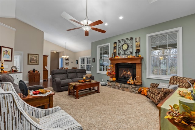 carpeted living room with ceiling fan with notable chandelier, a stone fireplace, and vaulted ceiling