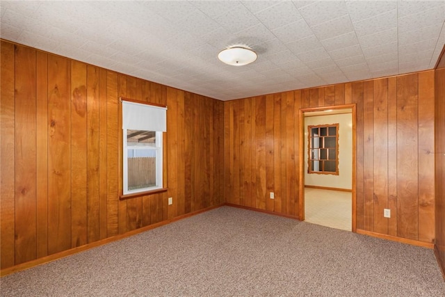 spare room featuring carpet flooring, baseboards, and wooden walls