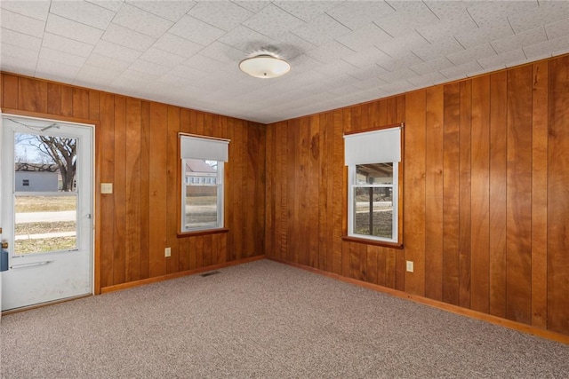 carpeted empty room featuring baseboards, plenty of natural light, wooden walls, and visible vents