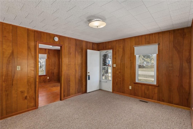 carpeted spare room with wooden walls, baseboards, and visible vents