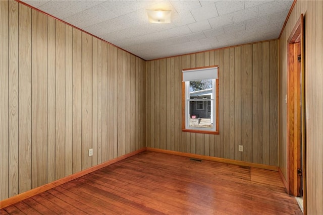 empty room featuring visible vents, wood finished floors, baseboards, and wood walls