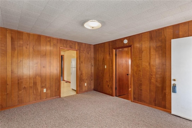 unfurnished bedroom with carpet floors, wooden walls, and freestanding refrigerator