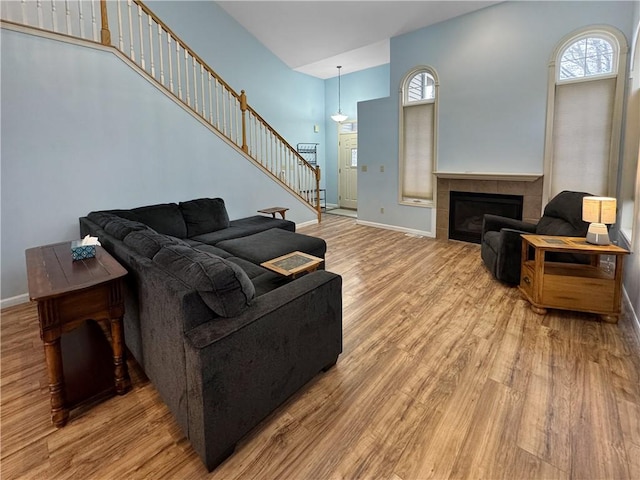 living room with a tiled fireplace, a towering ceiling, plenty of natural light, and light hardwood / wood-style floors