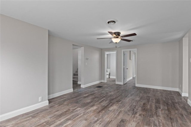 empty room featuring dark wood-style flooring, a ceiling fan, visible vents, baseboards, and stairway