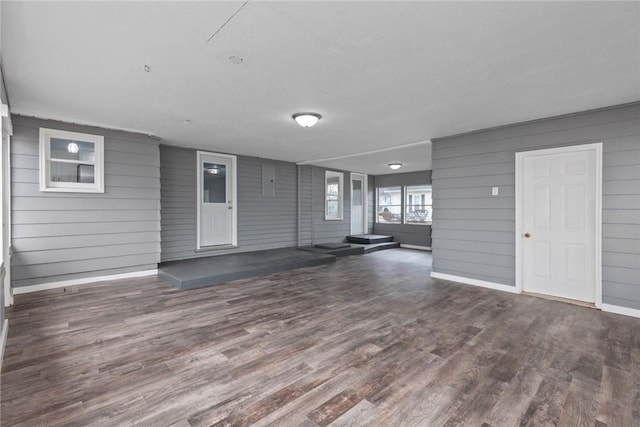 unfurnished living room with wood walls, baseboards, and dark wood finished floors