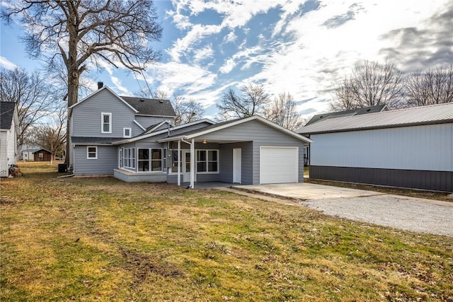 rear view of property featuring a garage, a sunroom, a yard, and driveway