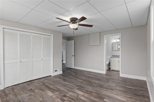 unfurnished bedroom with dark wood-style floors, a closet, a drop ceiling, and baseboards