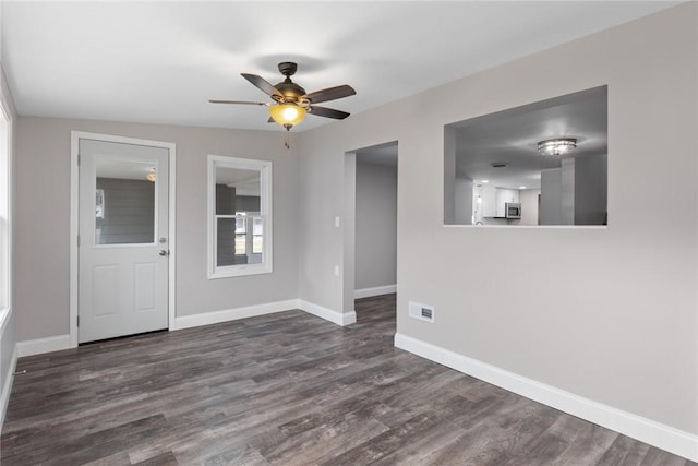 unfurnished room with dark wood-style floors, ceiling fan, visible vents, and baseboards