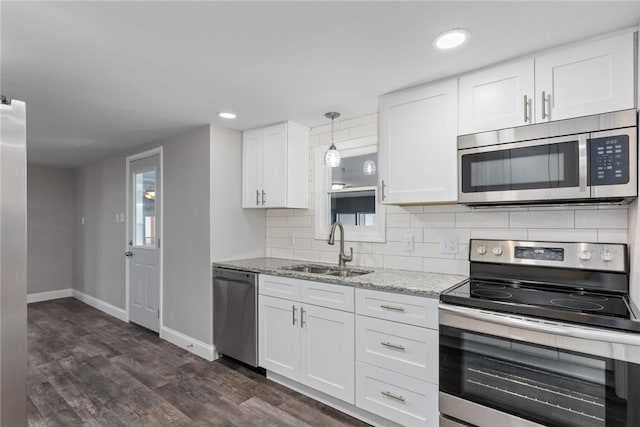 kitchen featuring appliances with stainless steel finishes, light stone countertops, white cabinetry, pendant lighting, and a sink