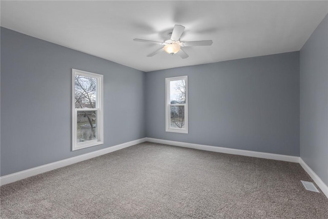 carpeted spare room featuring a wealth of natural light, visible vents, ceiling fan, and baseboards