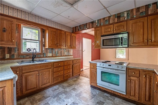 kitchen featuring white electric range, stainless steel microwave, a sink, a drop ceiling, and brown cabinets