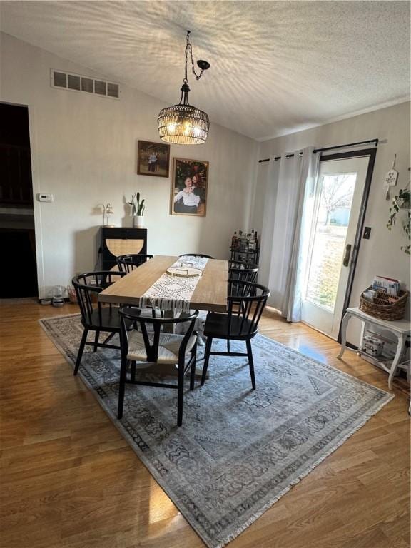 dining space with lofted ceiling, visible vents, a textured ceiling, and wood finished floors