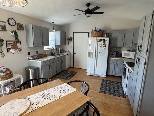 kitchen with lofted ceiling, gray cabinets, light countertops, a sink, and white appliances