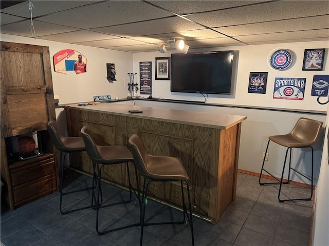 bar featuring dark tile patterned flooring, a dry bar, a drop ceiling, and baseboards